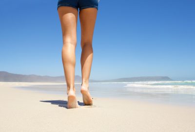 Female legs walking barefoot on beach from behind