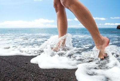 Side view barefoot female walking in water on black sand beach